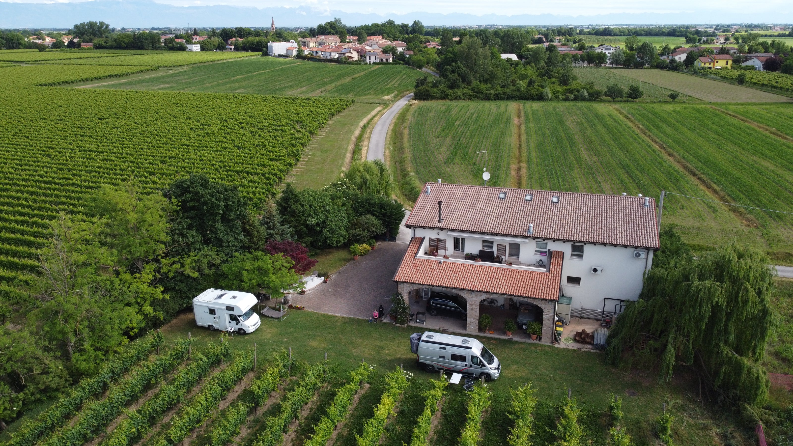Sfriso Winery seen from above from a drone showing the campers parked in front of the vineyard and the winery surrounded by green fields